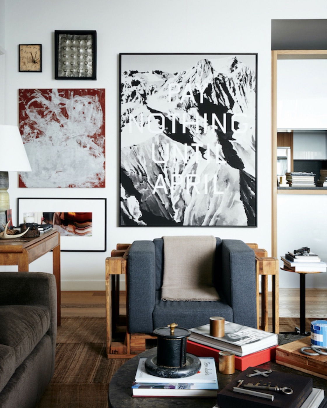 A living room with a large black and white mountain print, a grey armchair and a cluster of framed works