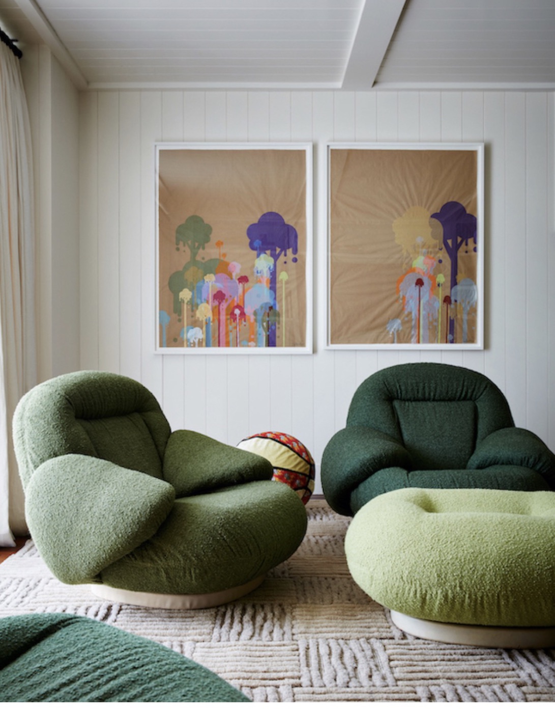 Two green bouclé lounge chairs below a pair of colourful framed prints