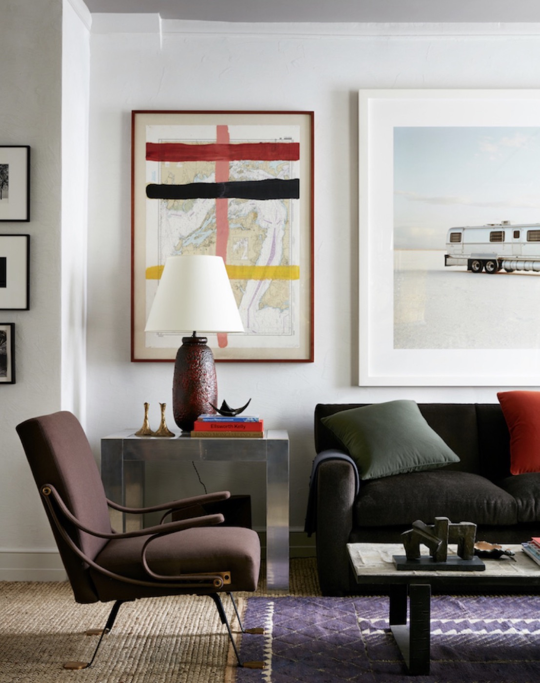 A dark sofa and brown lounge chair beneath framed works and a large photograph